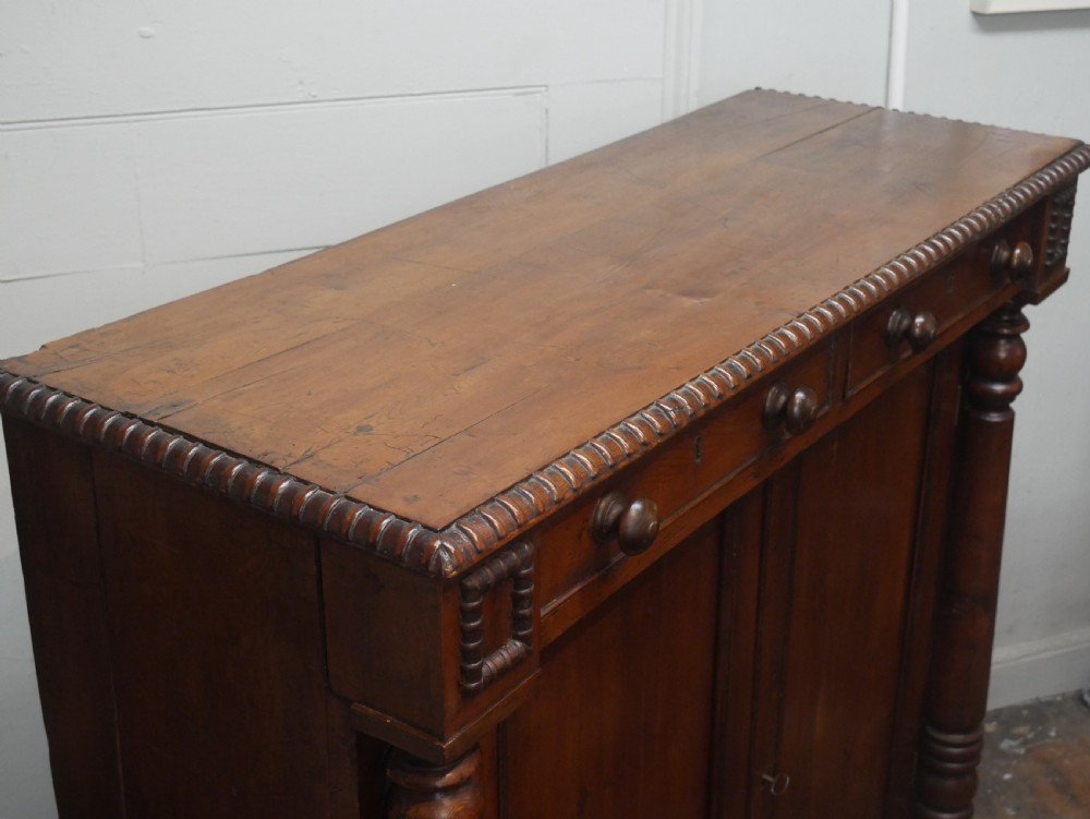 A warm brown cedar cupboard featuring two top drawers, twin panelled doors, and carved side columns supported by turned feet. View X