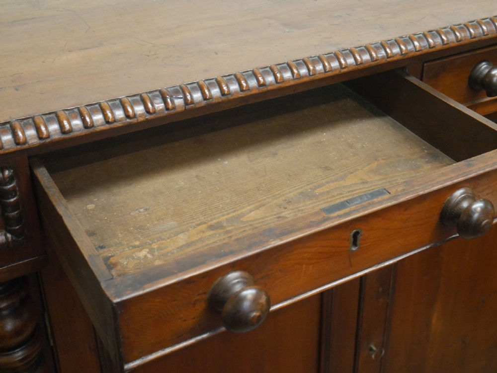 A warm brown cedar cupboard featuring two top drawers, twin panelled doors, and carved side columns supported by turned feet. View XIII