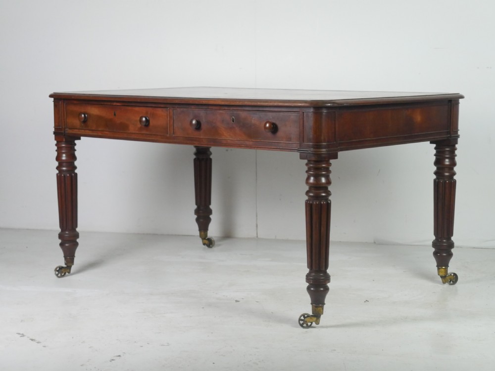 An antique Regency mahogany partners writing desk featuring turned fluted legs, brass castors, frieze drawers with wooden knobs, and a rectangular top.