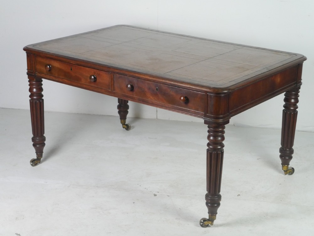 An antique Regency mahogany partners writing desk featuring turned fluted legs, brass castors, frieze drawers with wooden knobs, and a rectangular top. View II