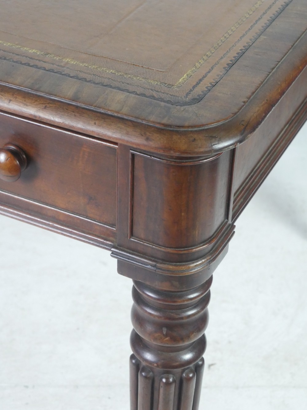 An antique Regency mahogany partners writing desk featuring turned fluted legs, brass castors, frieze drawers with wooden knobs, and a rectangular top. View III