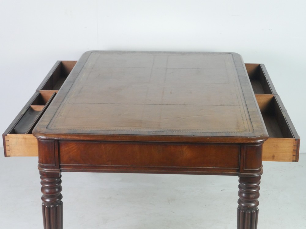 An antique Regency mahogany partners writing desk featuring turned fluted legs, brass castors, frieze drawers with wooden knobs, and a rectangular top. View IV