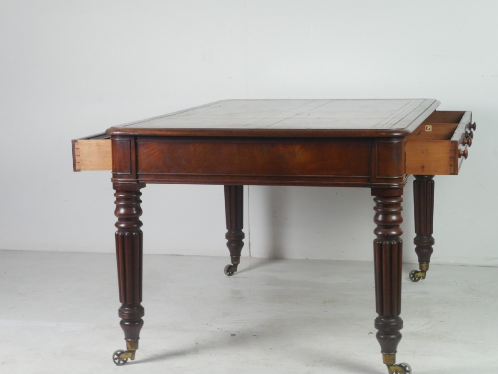 An antique Regency mahogany partners writing desk featuring turned fluted legs, brass castors, frieze drawers with wooden knobs, and a rectangular top. View V