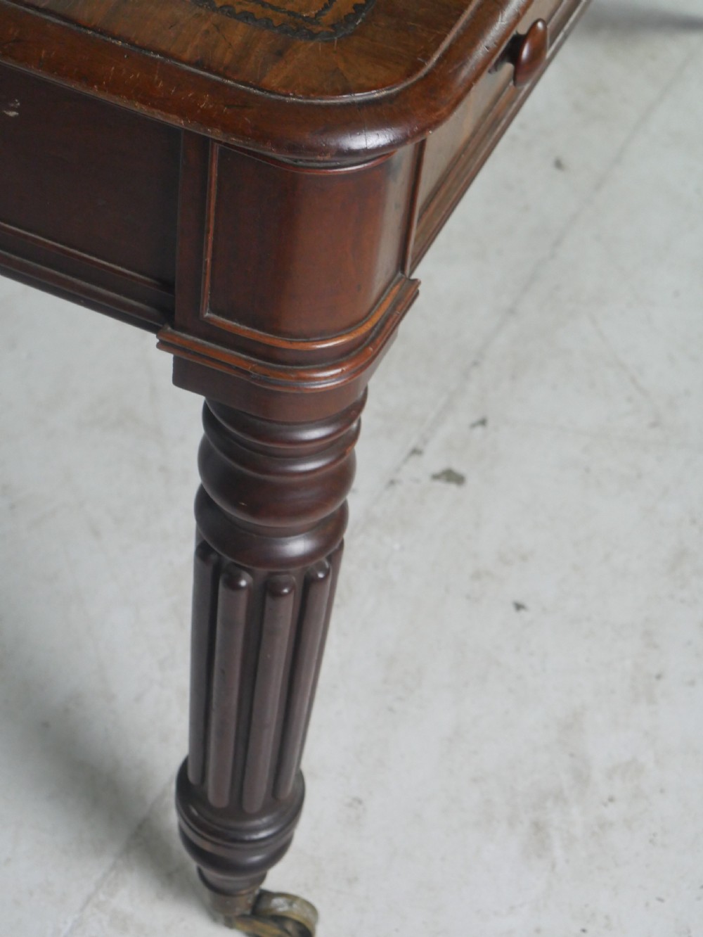 An antique Regency mahogany partners writing desk featuring turned fluted legs, brass castors, frieze drawers with wooden knobs, and a rectangular top. View VI