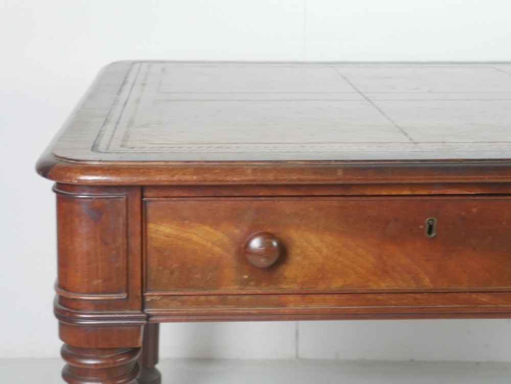 An antique Regency mahogany partners writing desk featuring turned fluted legs, brass castors, frieze drawers with wooden knobs, and a rectangular top. View VII