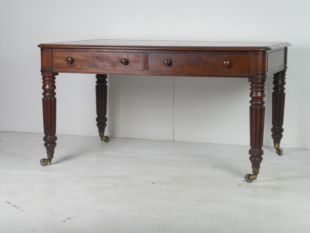 An antique Regency mahogany partners writing desk featuring turned fluted legs, brass castors, frieze drawers with wooden knobs, and a rectangular top. View X