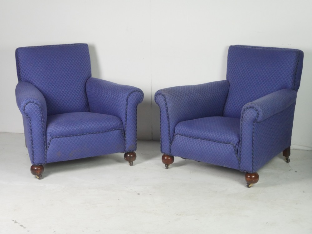 A pair of high-backed armchairs upholstered in patterned blue fabric with rolled arms and turned wooden feet on brass castors.