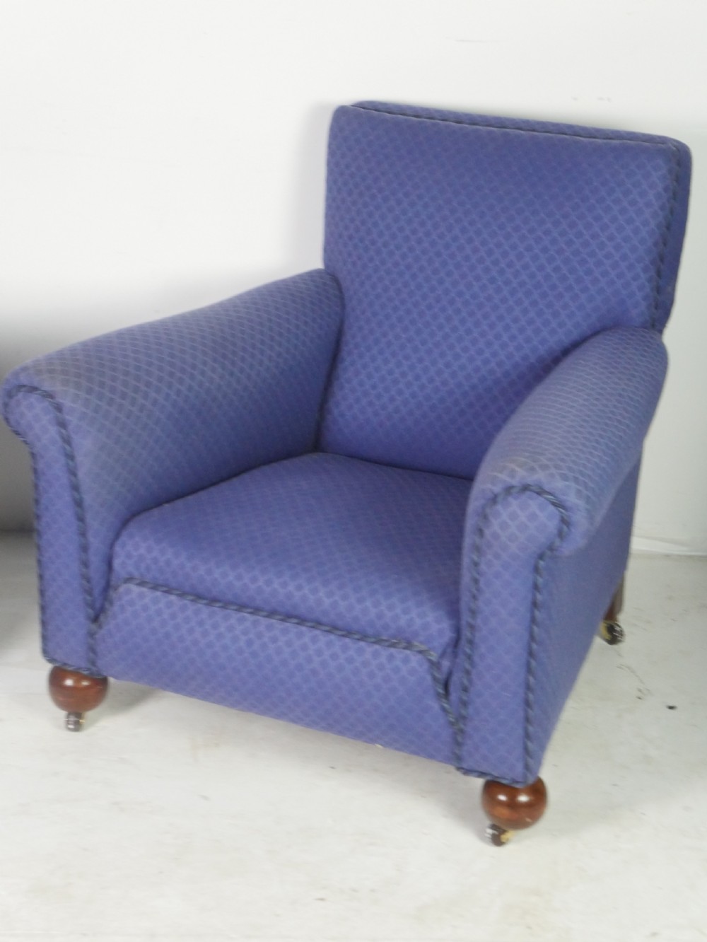 A pair of high-backed armchairs upholstered in patterned blue fabric with rolled arms and turned wooden feet on brass castors. View II