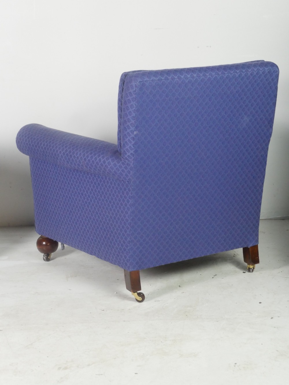 A pair of high-backed armchairs upholstered in patterned blue fabric with rolled arms and turned wooden feet on brass castors. View V