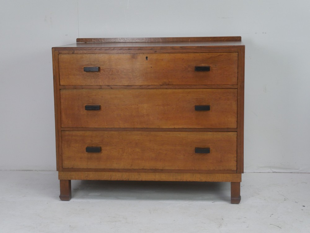 A mid-20th-century golden oak chest of drawers featuring three full-width drawers with contrasting dark wooden block handles and a low rear gallery rail. View II