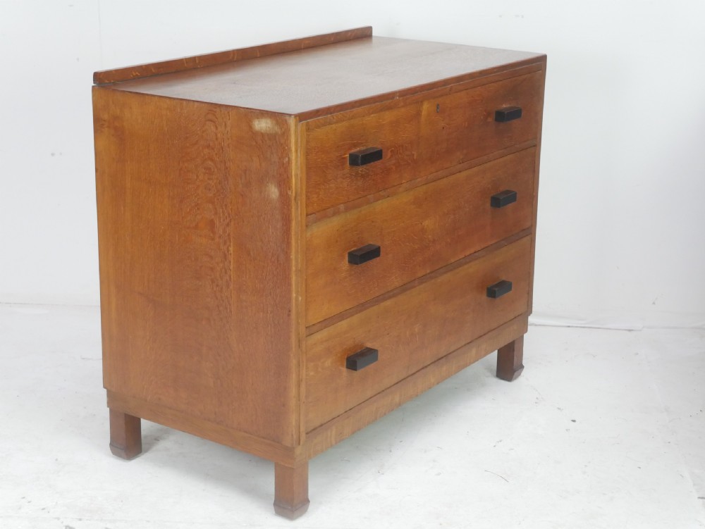 A mid-20th-century golden oak chest of drawers featuring three full-width drawers with contrasting dark wooden block handles and a low rear gallery rail. View IV