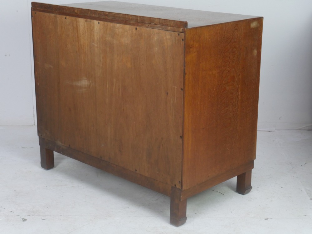 A mid-20th-century golden oak chest of drawers featuring three full-width drawers with contrasting dark wooden block handles and a low rear gallery rail. View VI