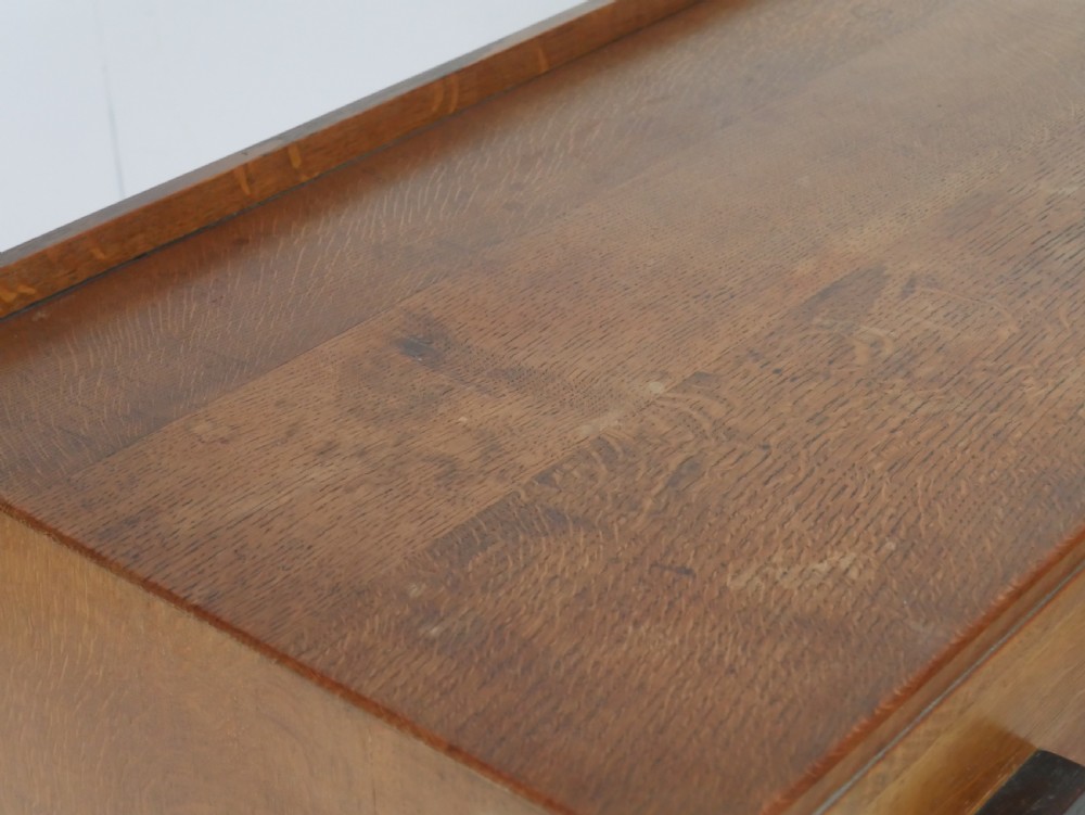 A mid-20th-century golden oak chest of drawers featuring three full-width drawers with contrasting dark wooden block handles and a low rear gallery rail. View X