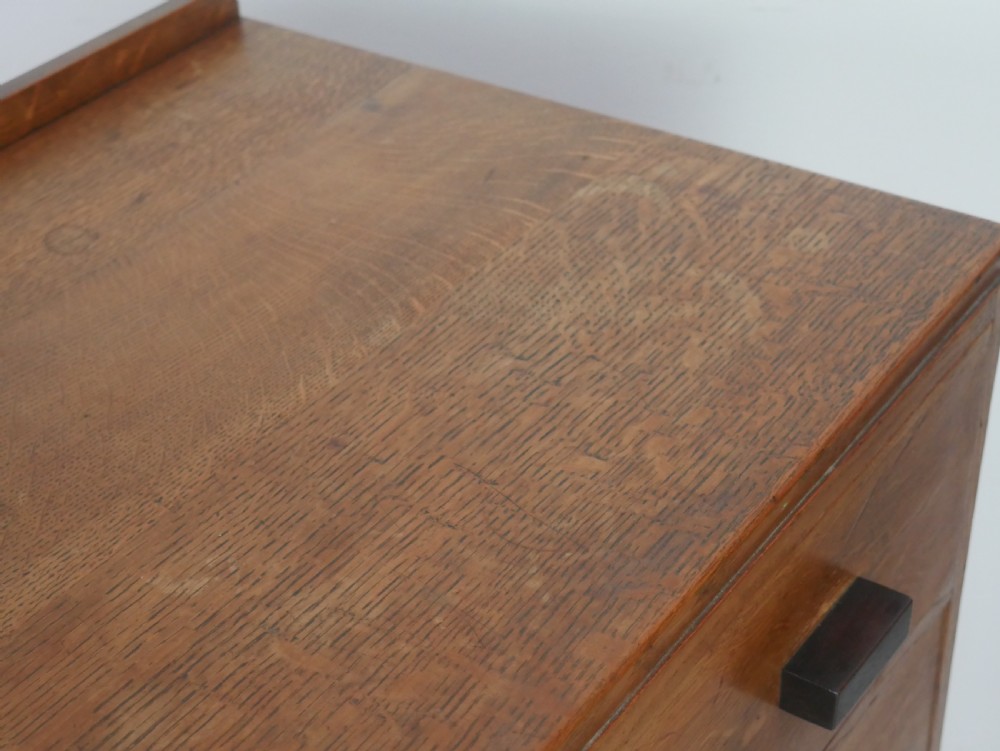 A mid-20th-century golden oak chest of drawers featuring three full-width drawers with contrasting dark wooden block handles and a low rear gallery rail. View XI