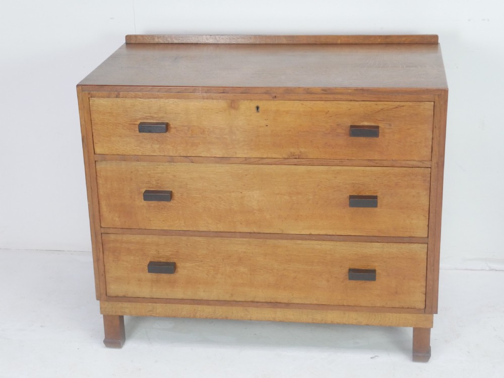 A mid-20th-century golden oak chest of drawers featuring three full-width drawers with contrasting dark wooden block handles and a low rear gallery rail. View XIII