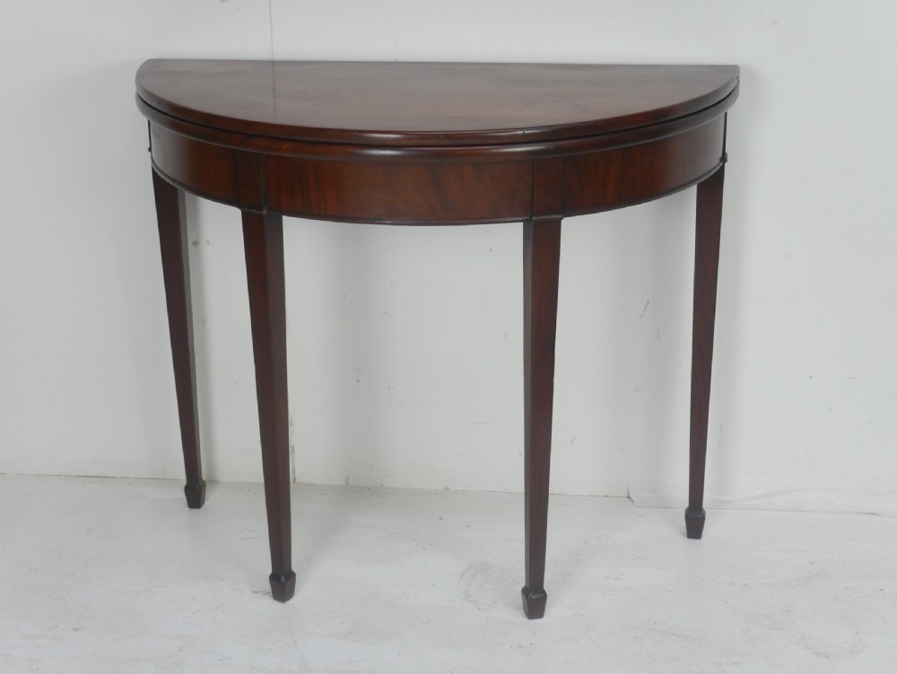 A Georgian mahogany demi-lune side table featuring a semi-circular top and four slender square tapered legs.