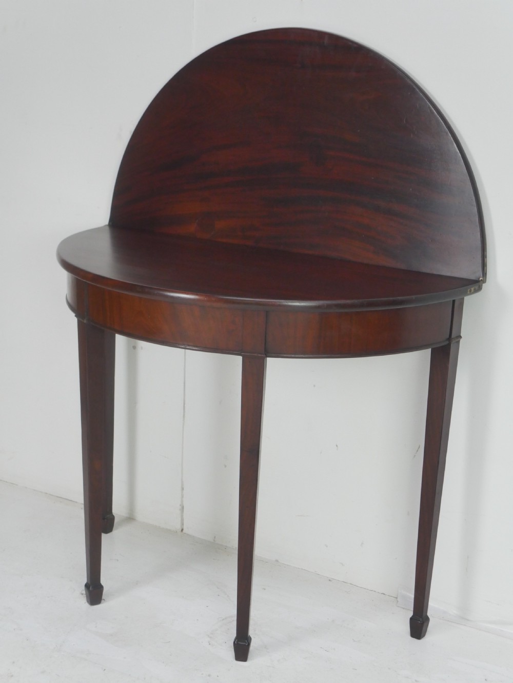 A Georgian mahogany demi-lune side table featuring a semi-circular top and four slender square tapered legs. View II