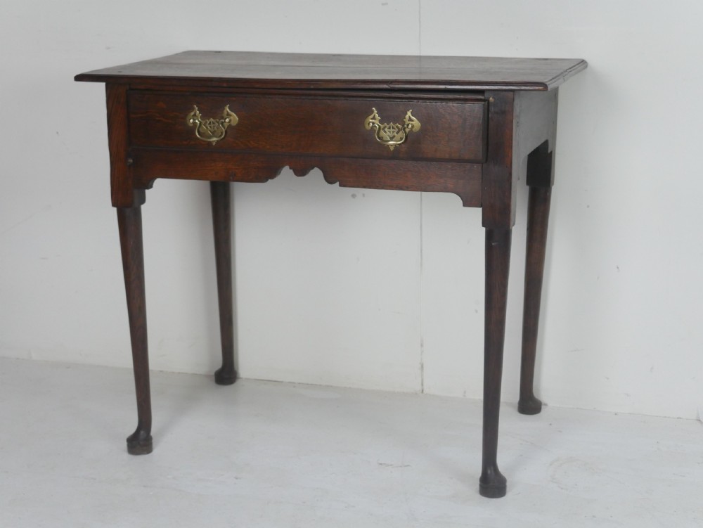 An antique dark oak side table featuring a single drawer with pierced brass handles, a shaped apron, and tapered legs ending in pad feet.