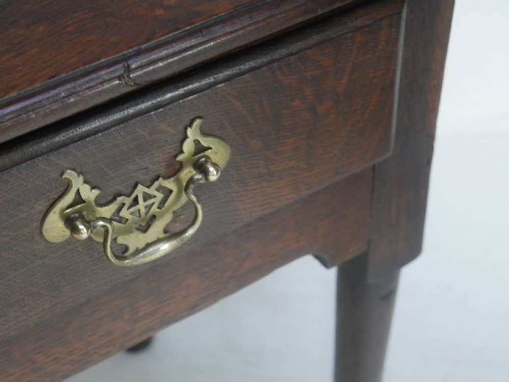 An antique dark oak side table featuring a single drawer with pierced brass handles, a shaped apron, and tapered legs ending in pad feet. View III