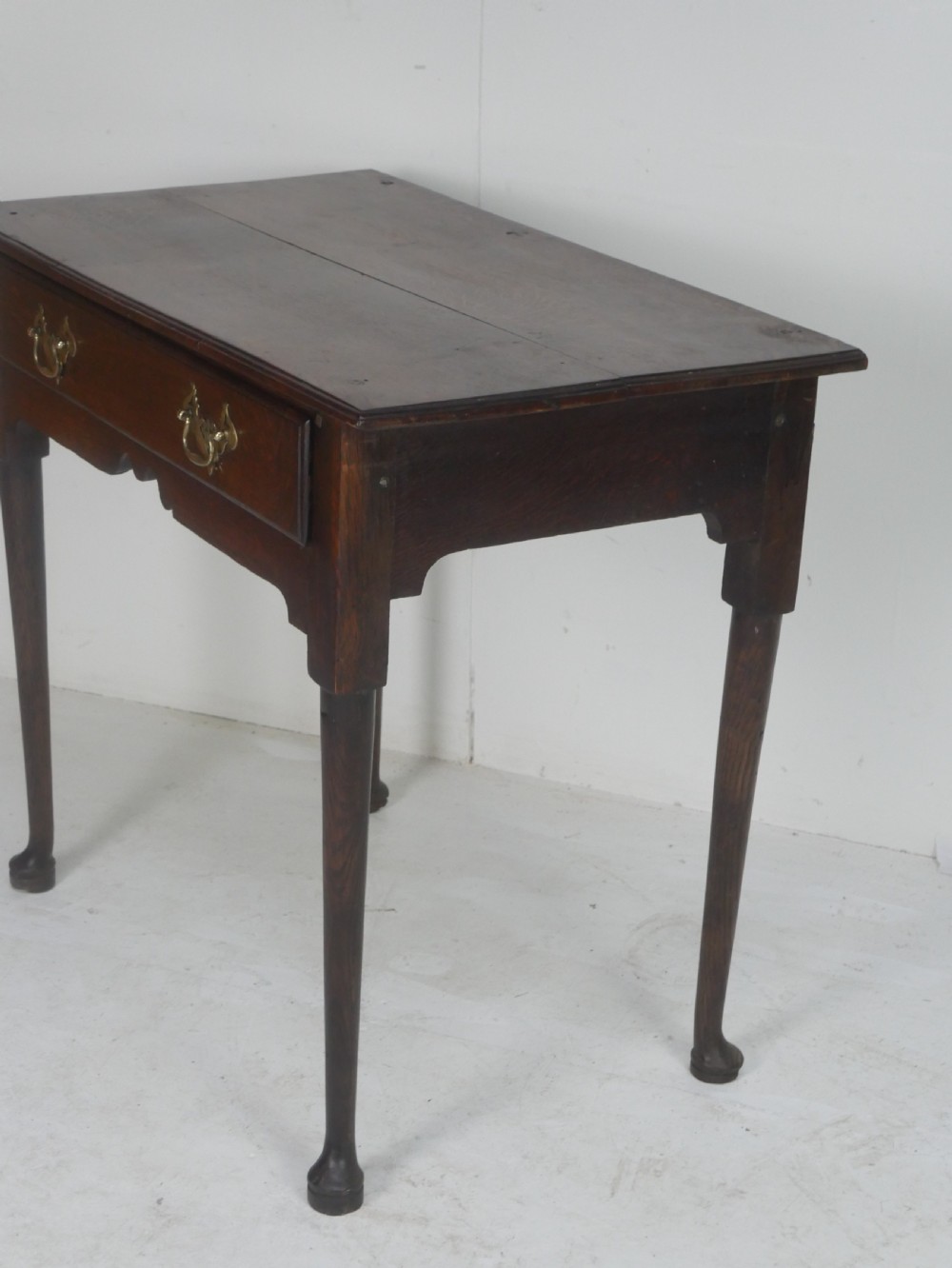 An antique dark oak side table featuring a single drawer with pierced brass handles, a shaped apron, and tapered legs ending in pad feet. View IV