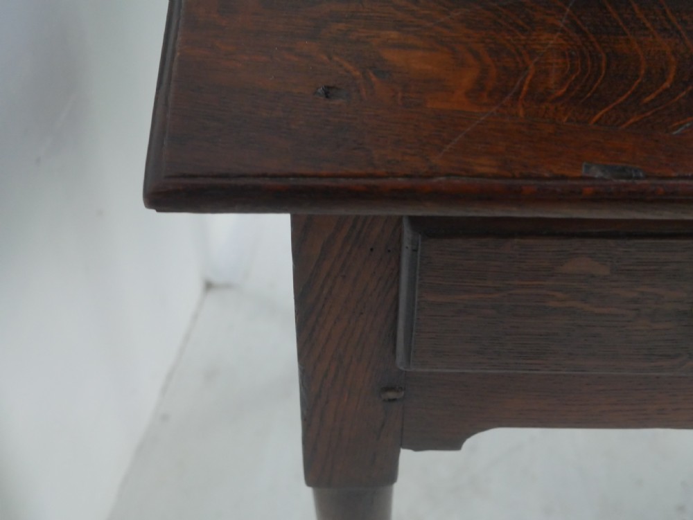An antique dark oak side table featuring a single drawer with pierced brass handles, a shaped apron, and tapered legs ending in pad feet. View VI
