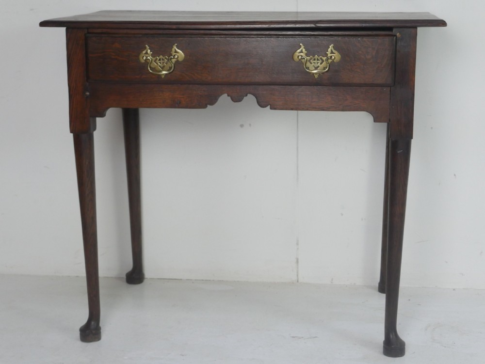 An antique dark oak side table featuring a single drawer with pierced brass handles, a shaped apron, and tapered legs ending in pad feet. View XII