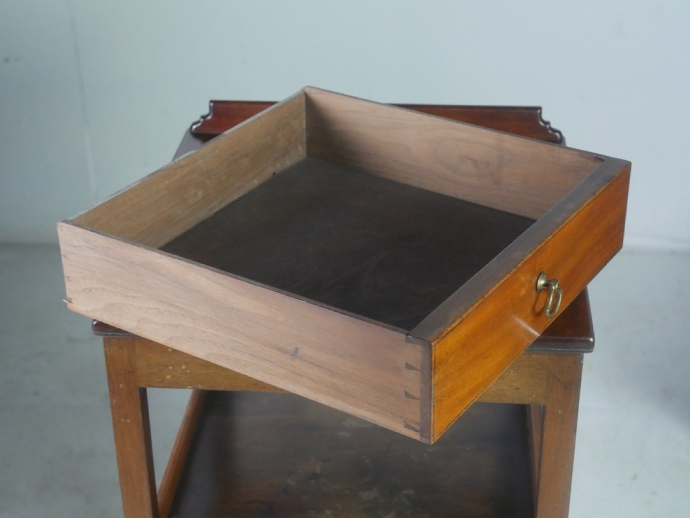 A narrow dark mahogany bedside table featuring a top surface with a gallery back, an open central shelf, a single drawer with a brass drop handle, and cross stretchers with a turned dish centre. View VIII