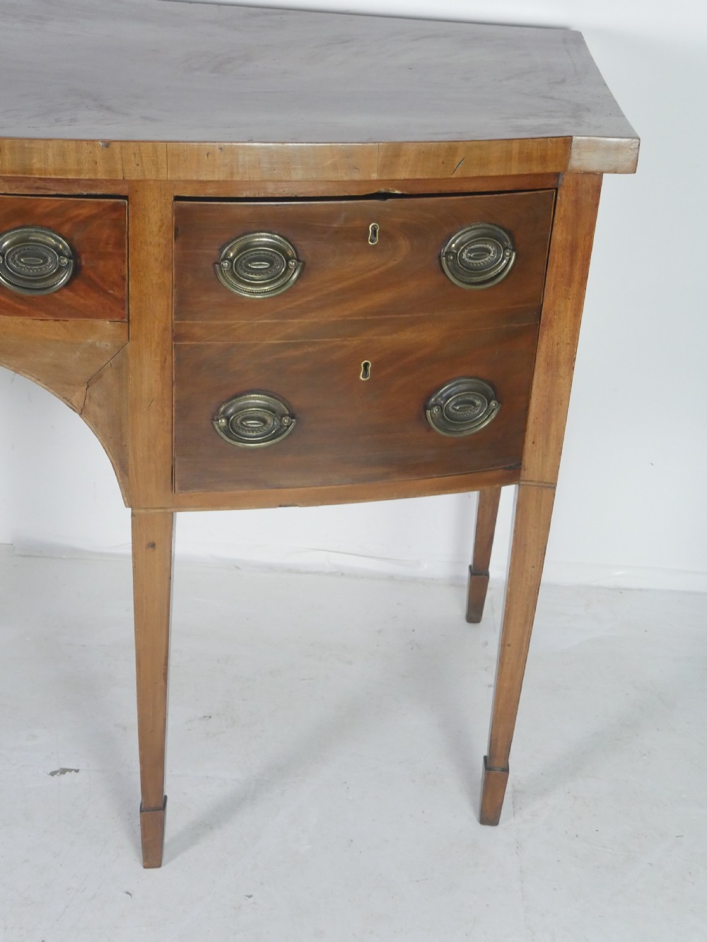A Georgian mahogany bow-front sideboard featuring a central arch aperture, multiple drawers with oval brass handles, and square tapered legs. View II