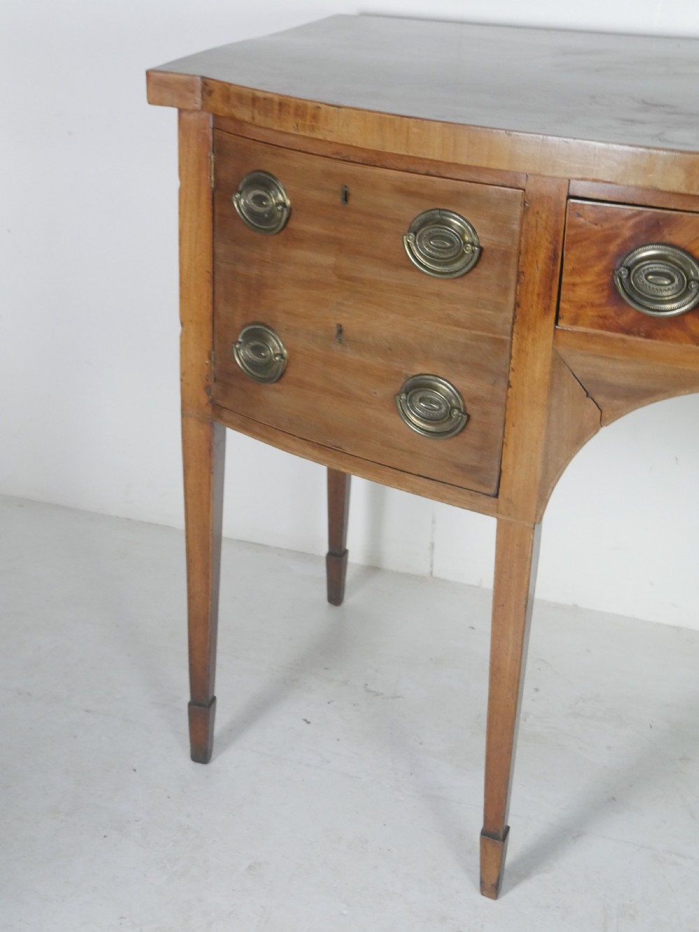 A Georgian mahogany bow-front sideboard featuring a central arch aperture, multiple drawers with oval brass handles, and square tapered legs. View IV