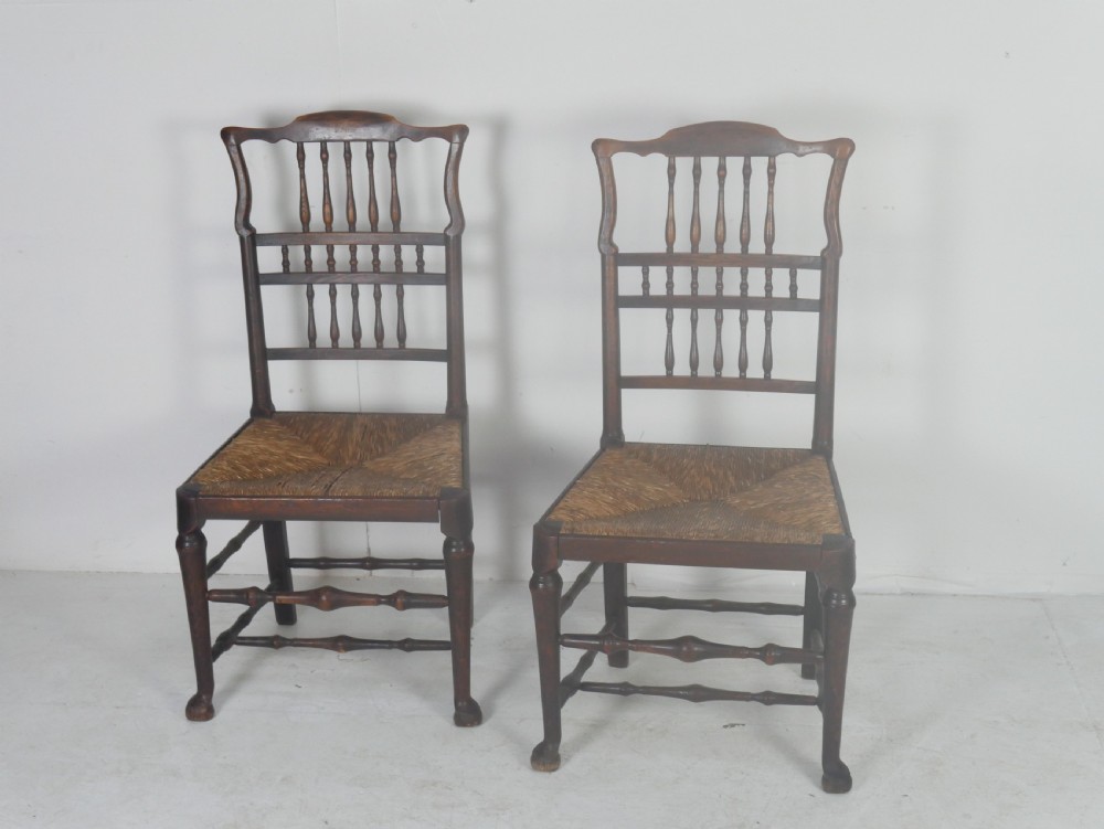 A pair of Georgian brown elm side chairs featuring spindle backrests, woven rush seats, and turned front legs.