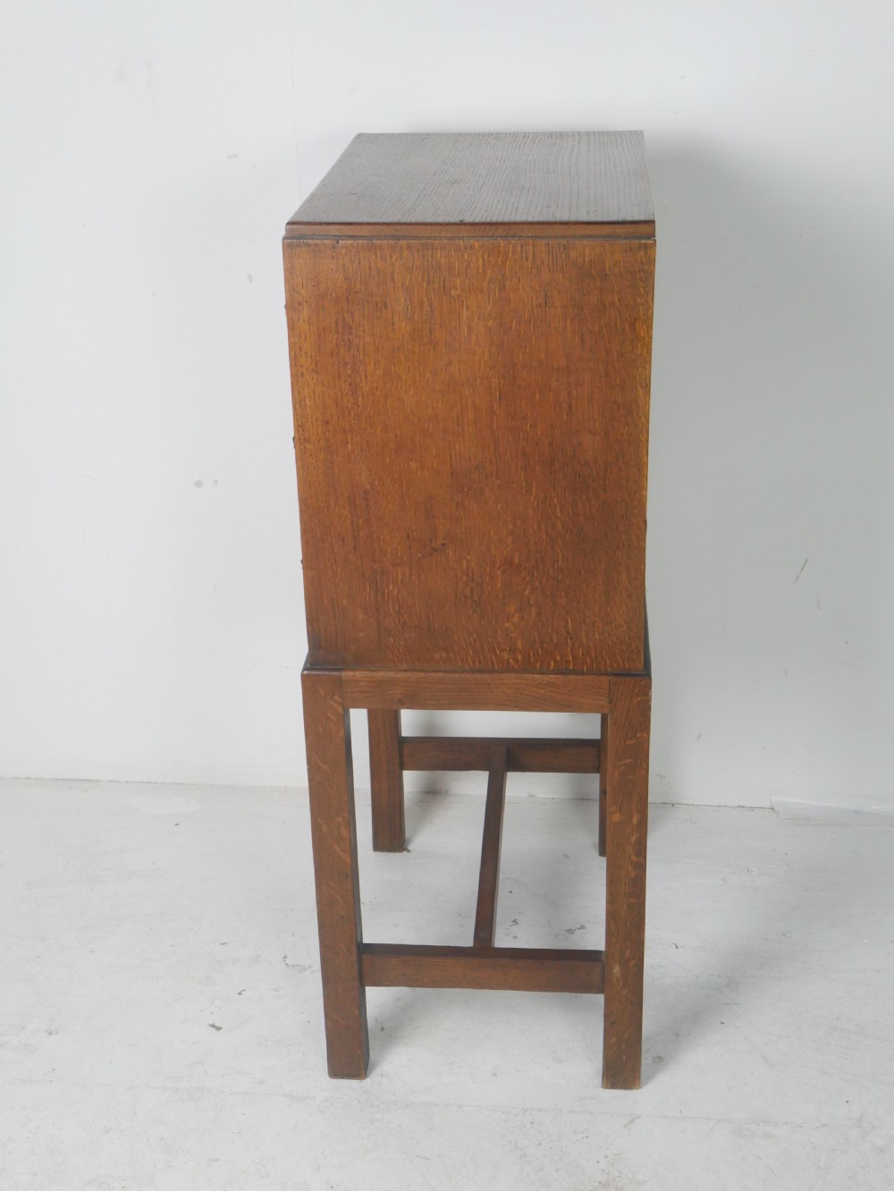 A small medium-brown oak chest featuring three drawers with brass lion mask ring handles, elevated on tall straight legs with an H-stretcher base. View IV