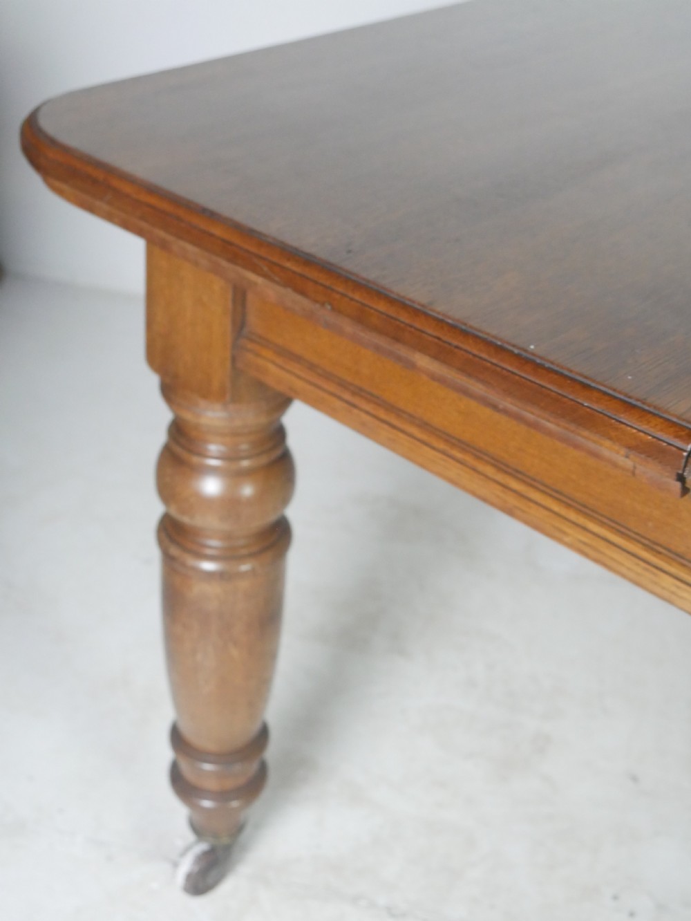 Victorian mahogany extending dining table resting on four turned legs with metal castors. View II