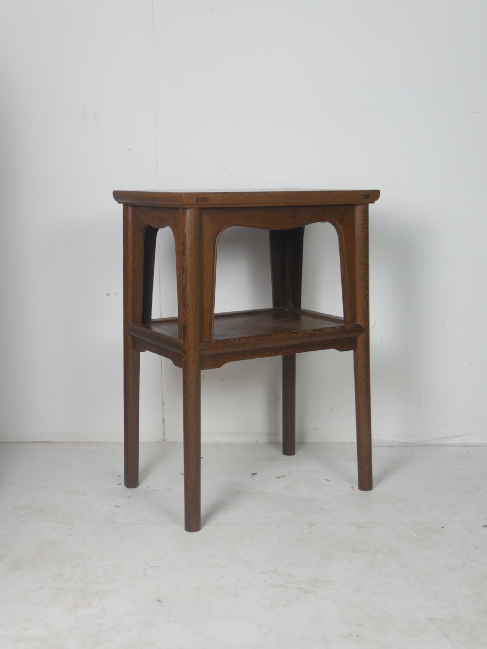 A warm brown oak side table featuring an upper rectangular top, arched aprons, a lower storage shelf, and straight legs.