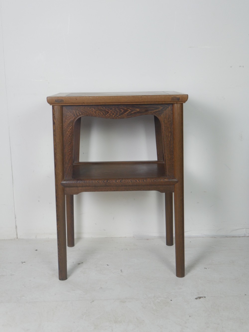 A warm brown oak side table featuring an upper rectangular top, arched aprons, a lower storage shelf, and straight legs. View VI