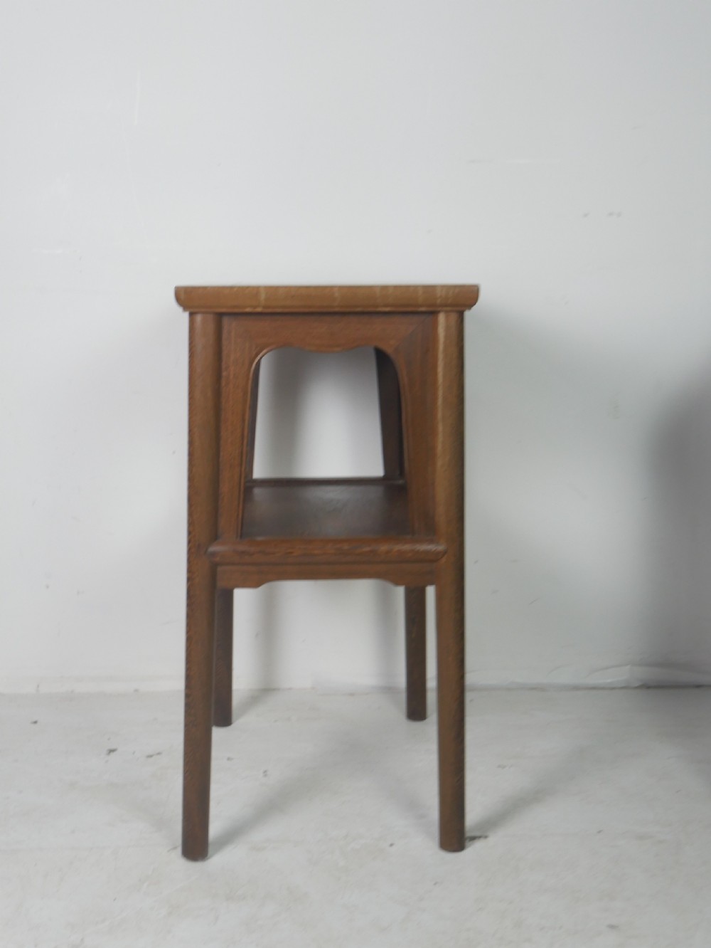 A warm brown oak side table featuring an upper rectangular top, arched aprons, a lower storage shelf, and straight legs. View VII