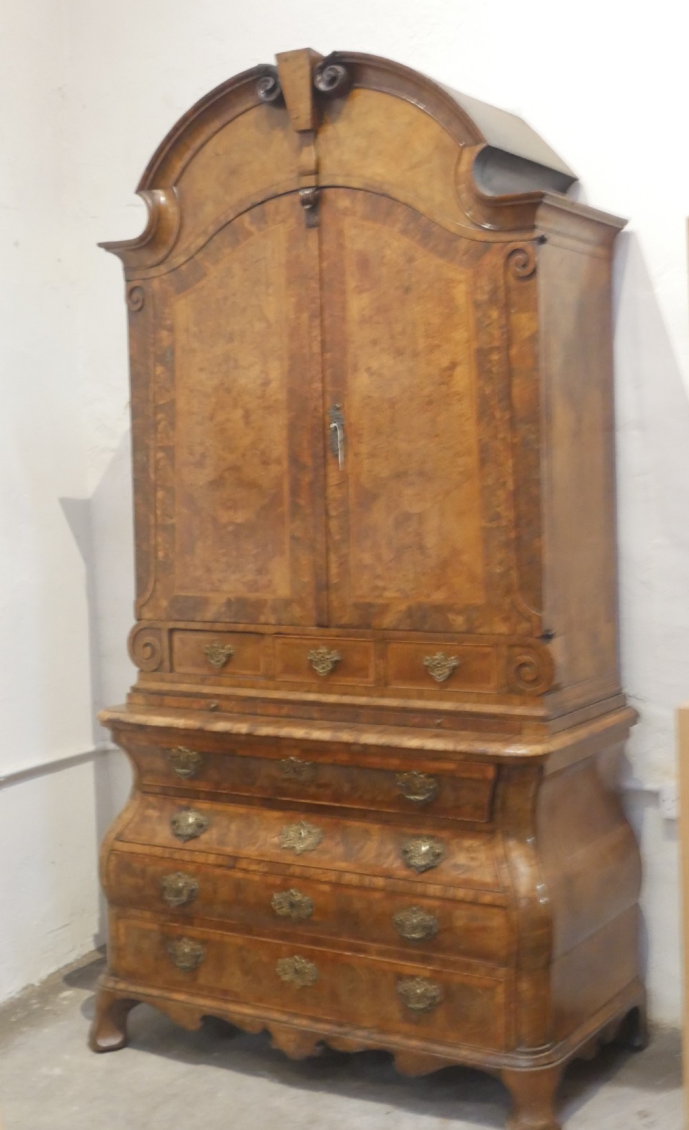 An 18th-century Dutch Rococo burr walnut cabinet featuring an arched moulded cornice, panelled doors, and a bombe three-drawer base with brass hardware. View II