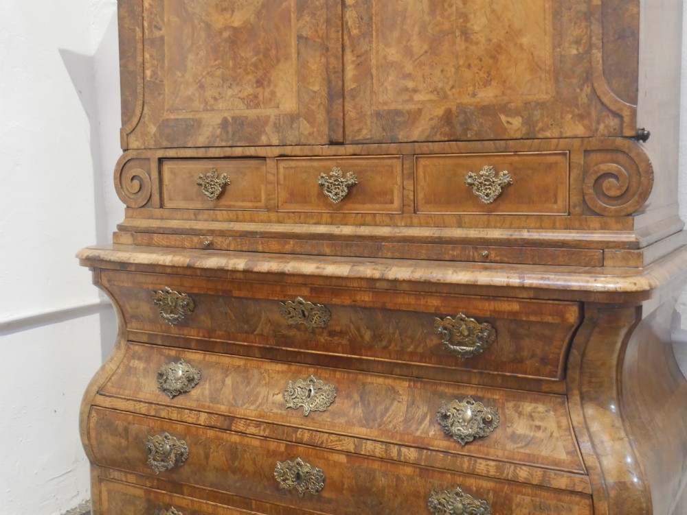 An 18th-century Dutch Rococo burr walnut cabinet featuring an arched moulded cornice, panelled doors, and a bombe three-drawer base with brass hardware. View VI