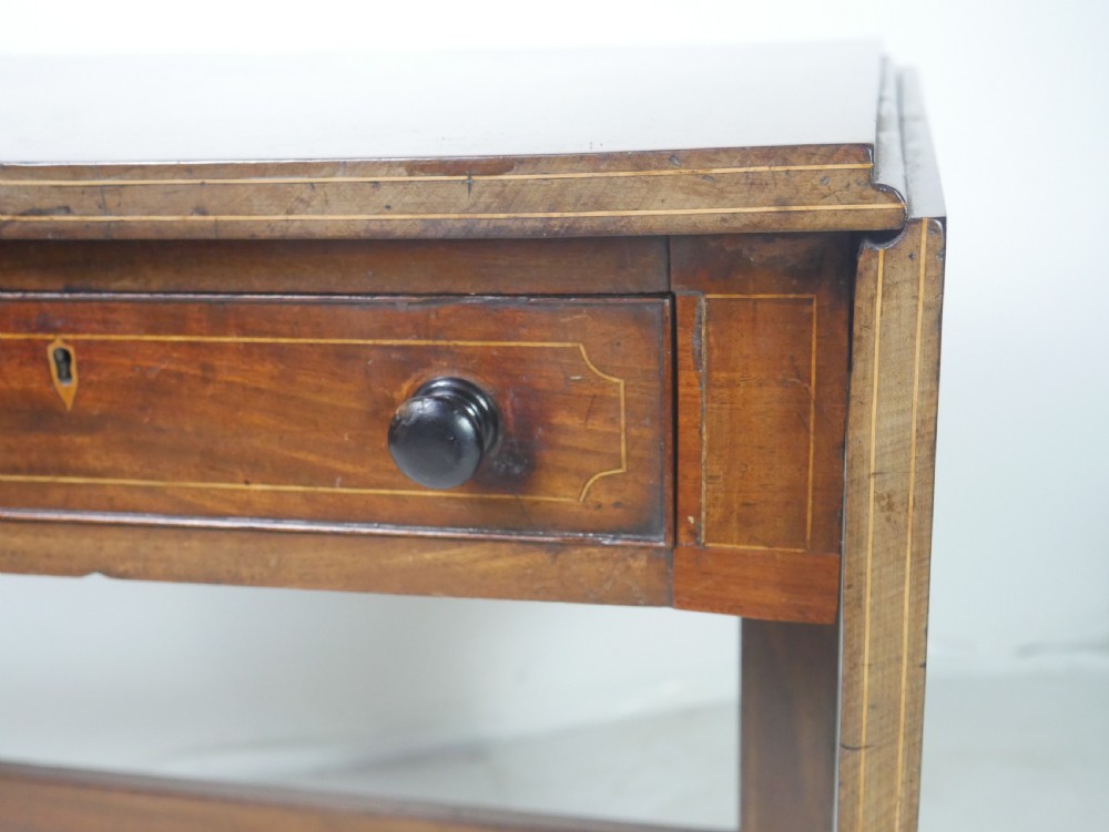 An antique Regency mahogany sofa table featuring two drop leaves, two frieze drawers with wooden knobs, and splayed legs with brass castors. View VI