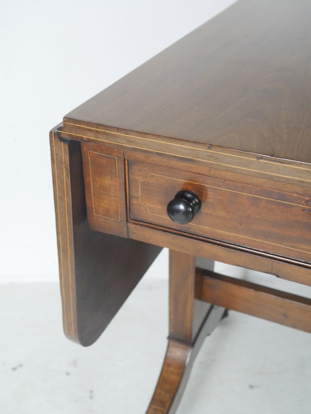 An antique Regency mahogany sofa table featuring two drop leaves, two frieze drawers with wooden knobs, and splayed legs with brass castors. View VII