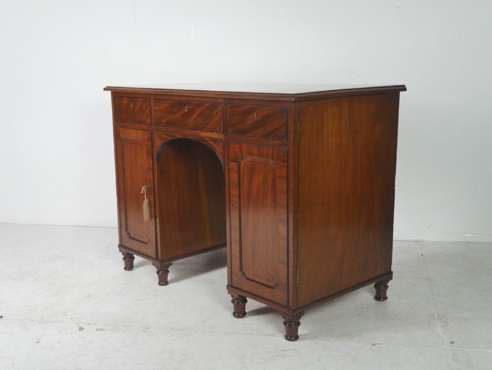 An antique mahogany kneehole dressing table featuring flame veneer drawer fronts, panelled cupboard doors, and turned feet.