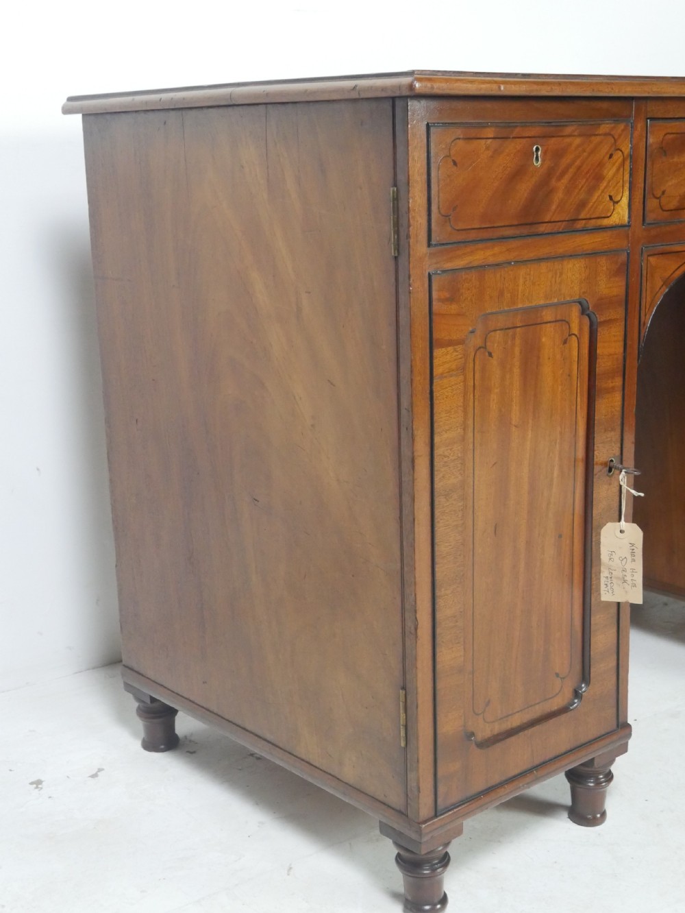 An antique mahogany kneehole dressing table featuring flame veneer drawer fronts, panelled cupboard doors, and turned feet. View II