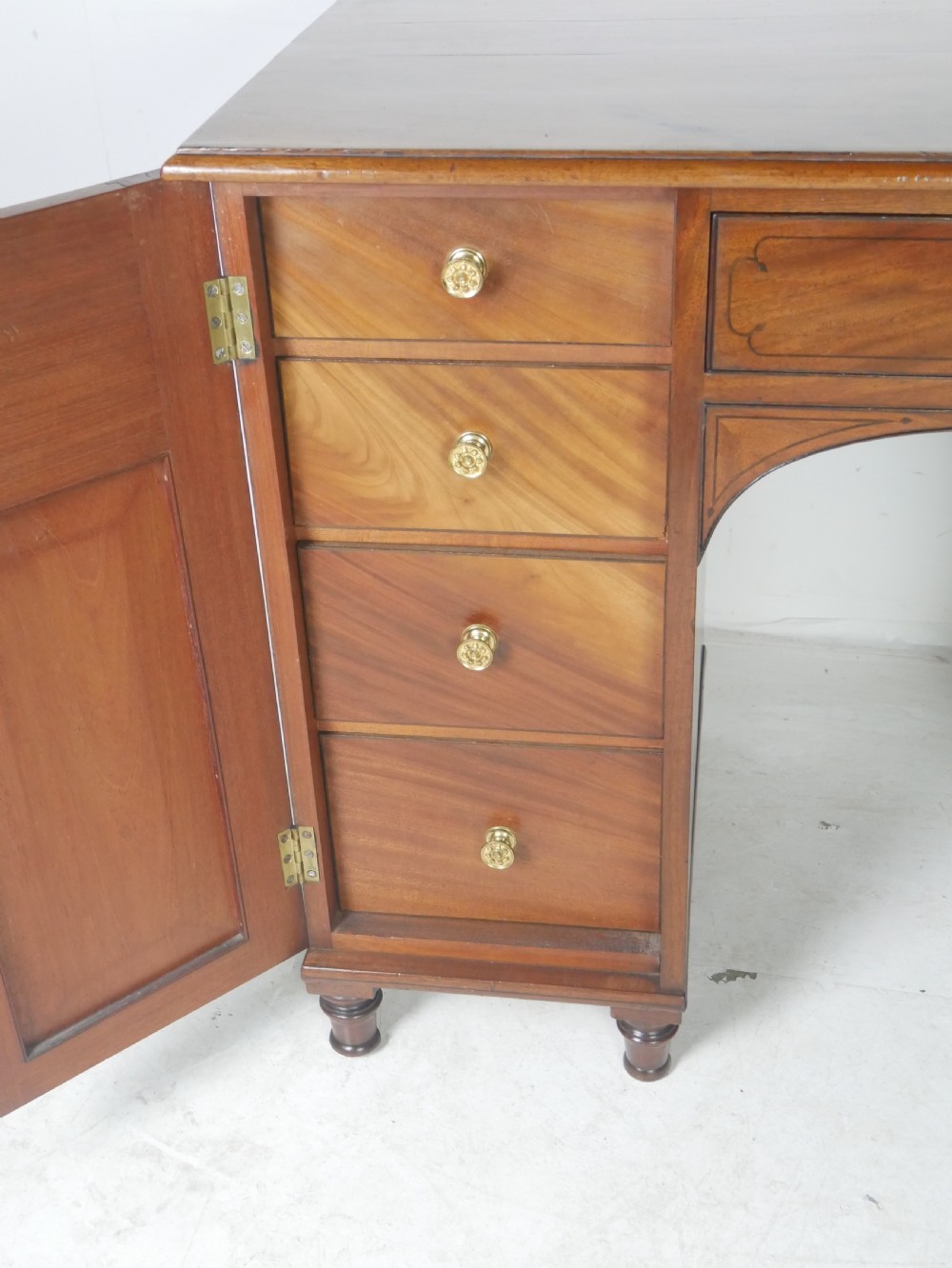 An antique mahogany kneehole dressing table featuring flame veneer drawer fronts, panelled cupboard doors, and turned feet. View III