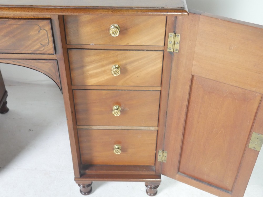 An antique mahogany kneehole dressing table featuring flame veneer drawer fronts, panelled cupboard doors, and turned feet. View IV