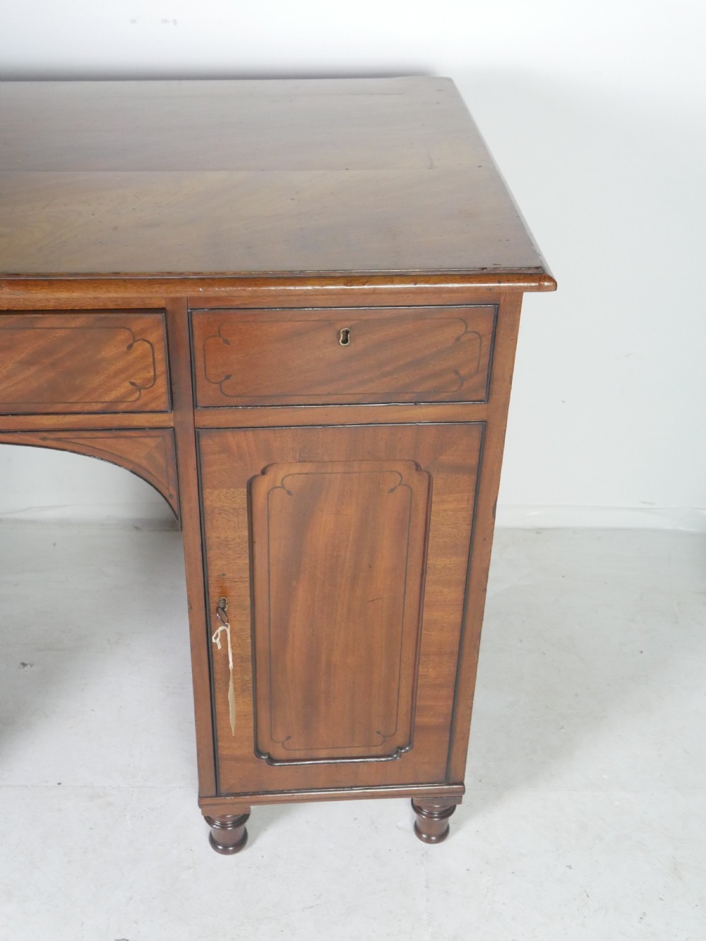 An antique mahogany kneehole dressing table featuring flame veneer drawer fronts, panelled cupboard doors, and turned feet. View V