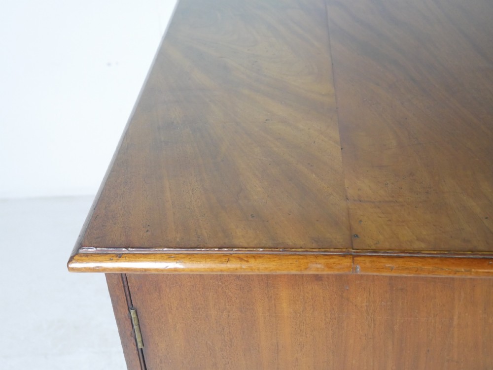 An antique mahogany kneehole dressing table featuring flame veneer drawer fronts, panelled cupboard doors, and turned feet. View VI