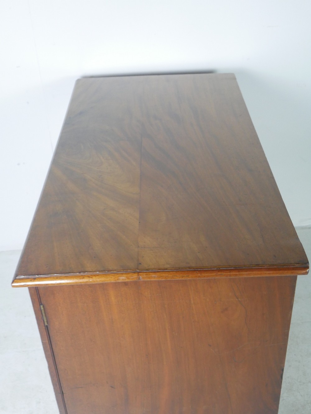 An antique mahogany kneehole dressing table featuring flame veneer drawer fronts, panelled cupboard doors, and turned feet. View VII