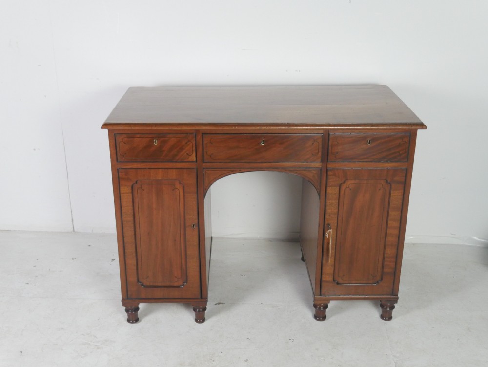 An antique mahogany kneehole dressing table featuring flame veneer drawer fronts, panelled cupboard doors, and turned feet. View XV
