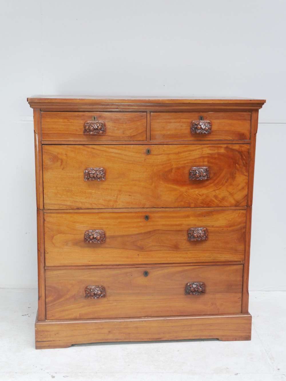 A 19th-century warm brown wooden tallboy chest featuring two short drawers over three long drawers with intricate carved foliate handles.