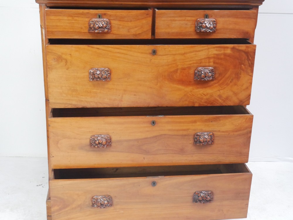 A 19th-century warm brown wooden tallboy chest featuring two short drawers over three long drawers with intricate carved foliate handles. View IV