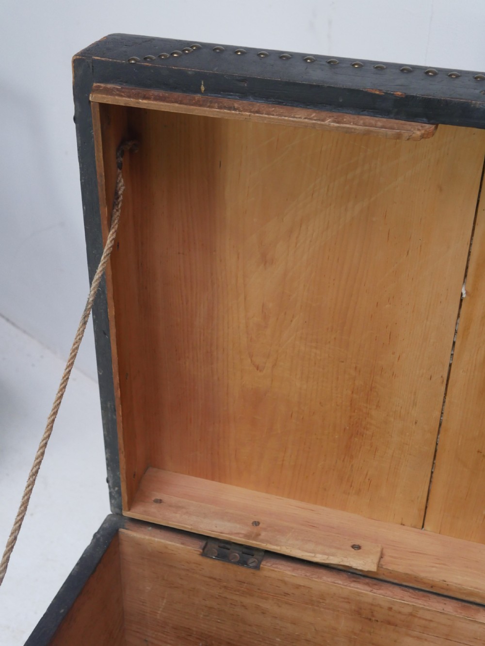 A black leather-covered storage trunk adorned with brass studding in festoon drape patterns, featuring side handles and castors. View II